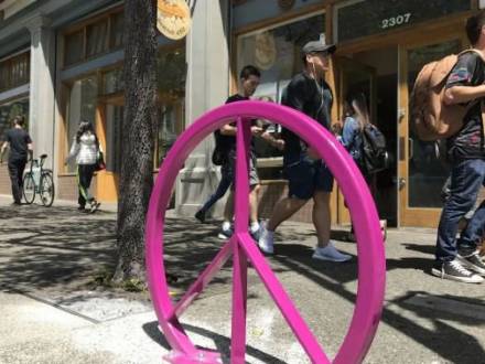 People walk by a hot pink peace sign sculpture in Berkeley