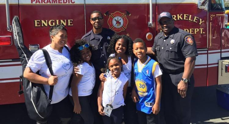 A family poses with two firefighters in uniform outside of a red firetruck at the Berkeley Juneteenth Festival. 