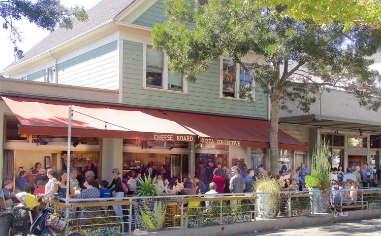 A large crowd gathers outside of Cheese Board Pizza Collective near North Berkeley BART Station
