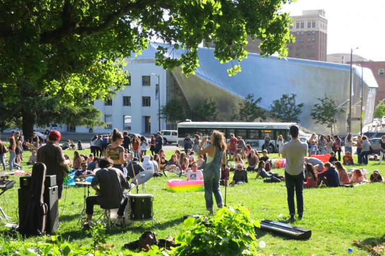A band performs in a park outside of Berkeley Art Museum and Pacific Film Archive in front of an audience on blankets.