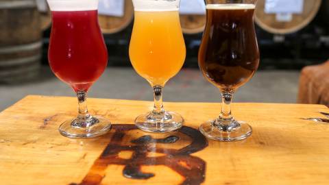 A flight of three beers on table, one auburn in color, another golden, and the last dark from Rare Barrel in Berkeley CA