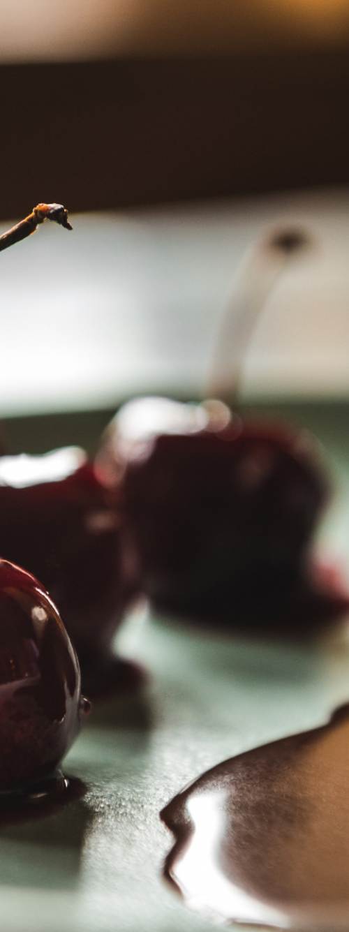 A chocolate cake dessert, topped with a scoop of ice cream and chocolate syrup, sits on a plate next to cherries.