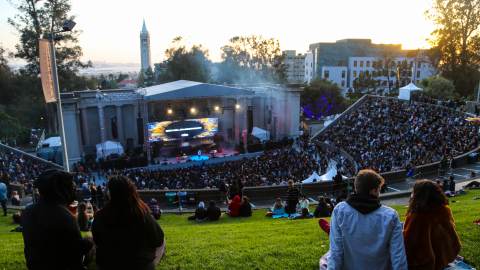 People sit on the lawn and look down at the band playing at Greek Theatre Sunset Hill in Berkeley, CA