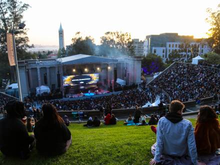 People sit on the lawn and look down at the band playing at Greek Theatre Sunset Hill in Berkeley, CA