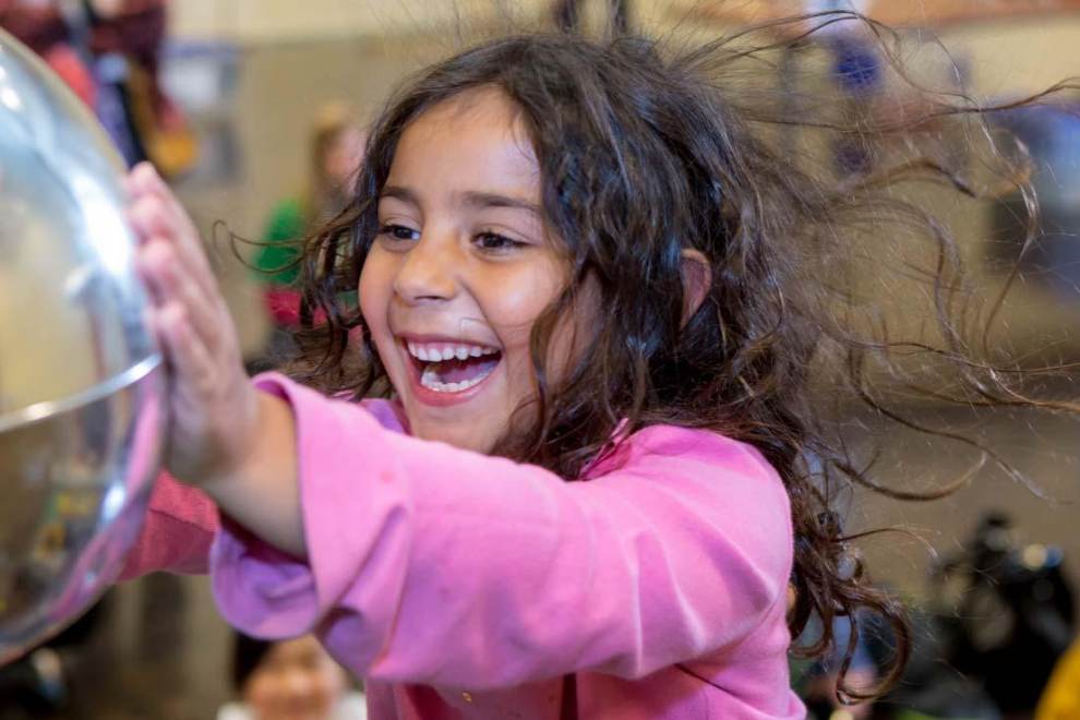 a child in a pink sweater touches a mirrored orb at the Lawrence Hall Of Science in Berkeley, CA