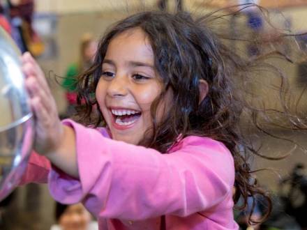 a child in a pink sweater touches a mirrored orb at the Lawrence Hall Of Science in Berkeley, CA